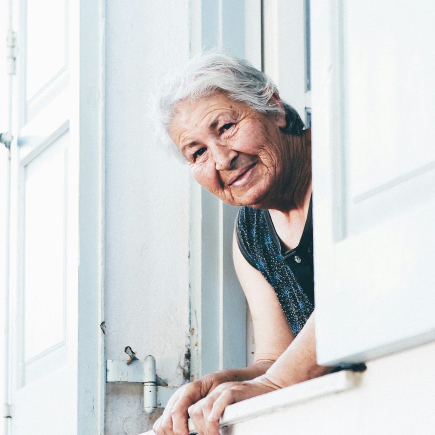 Eine ältere Dame lehnt lächelnd aus einem geöffneten Fenster